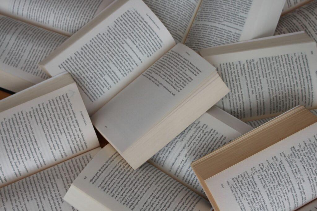 Scattered pile of open books showing black text on white backgrounds.